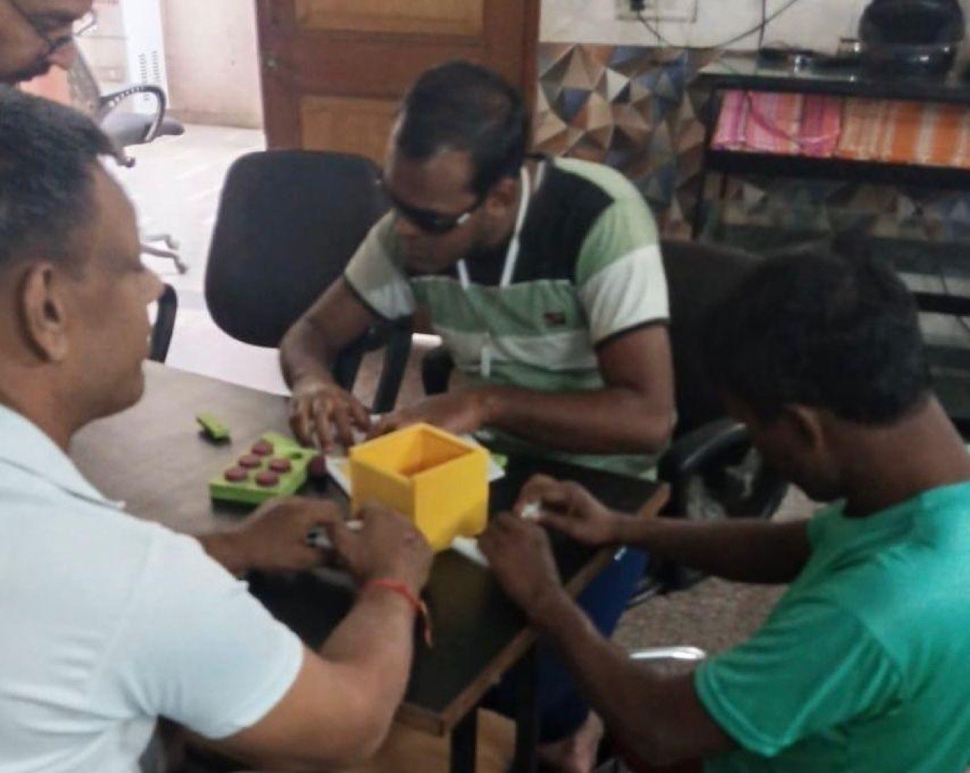 Learners at Divya Jyoti Niwas seated around a table, hands on the Math Kit&rsquo;s Braille number tiles while an educator leans in to help.