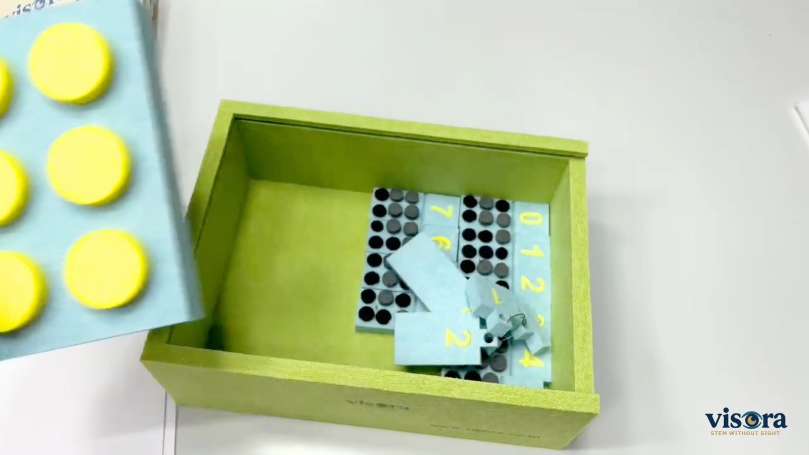 The Math Kit in its green box: Braille number tiles, a tactile counting board and measurement pieces.